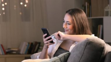 Gece evde TV içerik paylaşmak için akıllı telefon kullanan mutlu kadın