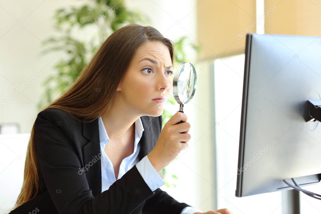 Suspicious office worker checking online content on computer using a magnifying glass