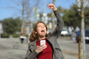 Çevrimiçi iyi haberi kutlayan heyecanlı gençler ellerinde akıllı bir telefonla caddede