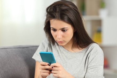 Evde oturma odasındaki kanepede oturan akıllı telefon içeriğini kontrol eden bağımlı bir genç.