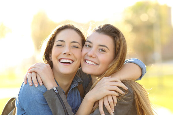 Front view portrait of a happy friends with perfect smile cuddling looking at you in a park at sunset