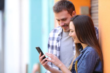 Mutlu çift sokakta bir duvarındaki eğilerek akıllı telefon içeriğini görüntülemek