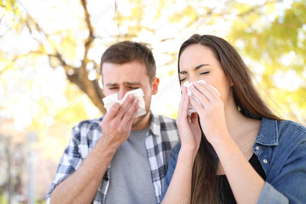 Sick couple sneezing together covering mouth with wipes in a park