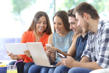 Mutlu arkadaş grubu evdeki oturma odasındaki koltukta oturan birden fazla cihazı kontrol ediyor.