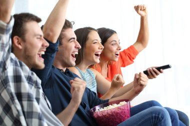 Dört heyecanlı arkadaş TV izlerken başarıyı kutluyorlar evde bir kanepenin üzerinde oturuyorlar