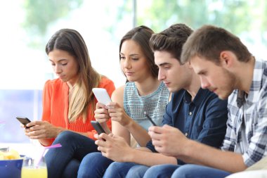 Oturma odasında evde bir kanepede oturan akıllı telefonlarını kullanarak ciddi arkadaş grubu