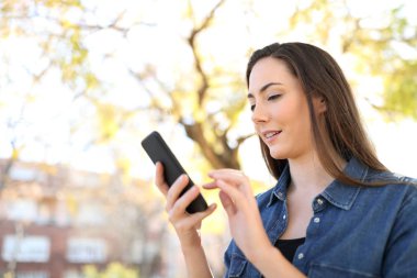 Parkta yürürken akıllı telefon kullanan bir kadının profili