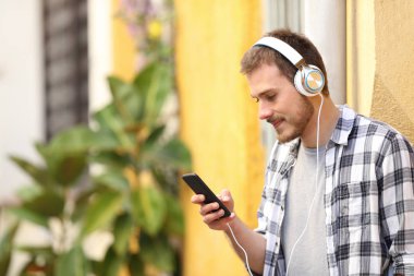 Ciddi bir adam sokakta duran akıllı telefon ve kulaklıklardan müzik dinliyor.
