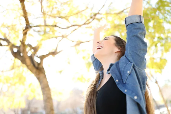 兴奋的女人举起双臂庆祝在一个以树木为背景的公园里的成功 — 图库照片