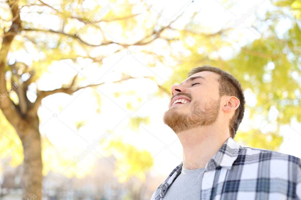 Happy man is breathing fresh air in a park with trees in the background