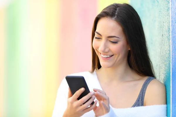 Happy woman is browsing smart phone side a colorfull wall — Stok Foto