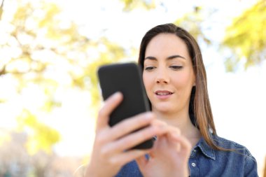 Akıllı telefon kullanan kadın bir parkta yürüyor