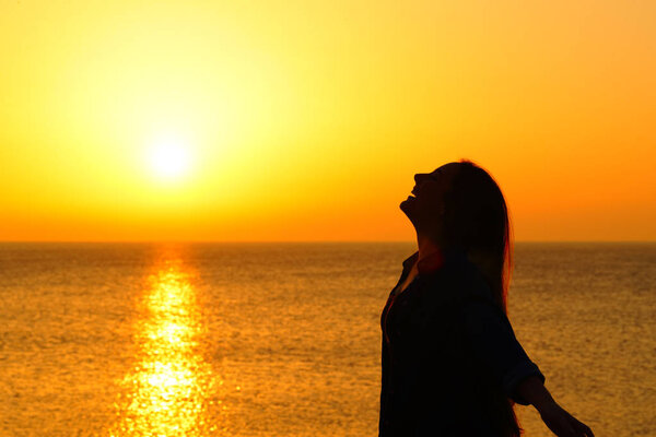 Happy woman on the beach breathing at sunset