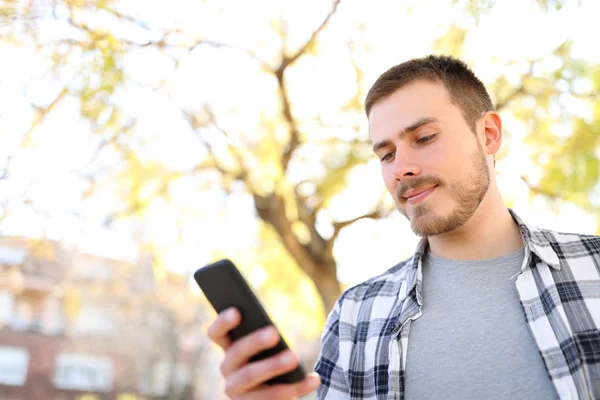 Hombre serio utiliza un teléfono inteligente caminando en un parque —  Fotos de Stock