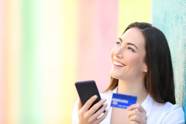 Online shopper thinking holding phone and credit card — Stock Photo, Image