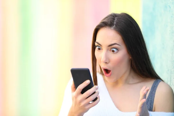 Здивована дівчина знаходить вміст телефону на барвистій вулиці — стокове фото