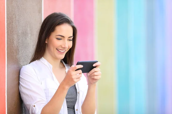 Glad tjej tittar på videor på smart telefon i en färgglad gata — Stockfoto