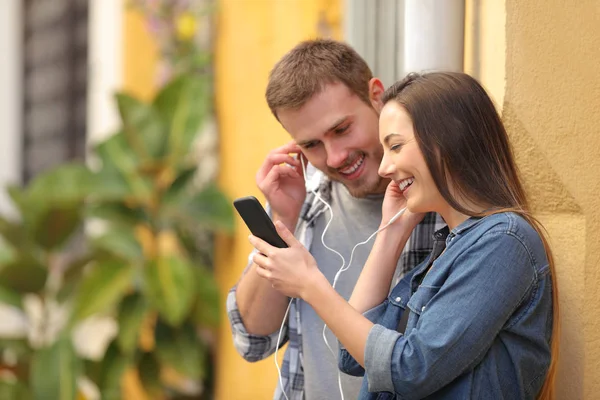 Pareja compartiendo auriculares para ver los medios en el teléfono — Foto de Stock