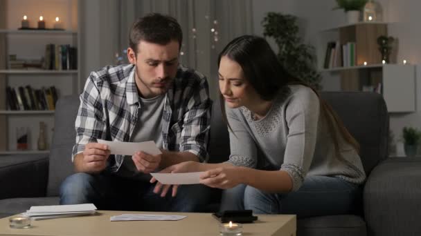 心配しているカップルの夜自宅でソファに座って銀行の領収書をチェック — ストック動画