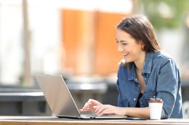 Bir tablo bir parkta otururken bir dizüstü bilgisayar kullanan mutlu kadın