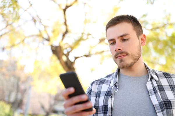 Allvarlig man använder en smart telefon som promenader i en park — Stockfoto