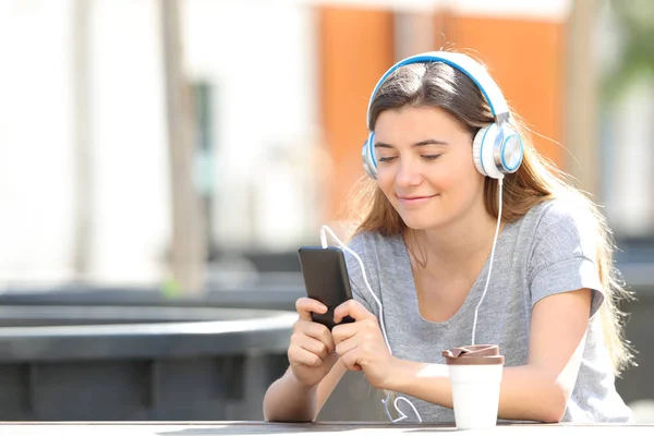 10 代の少女が公園で携帯電話を使用して音楽を聴く — ストック写真