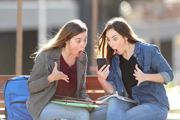 Dos estudiantes asombrados revisando el contenido del teléfono en un parque — Foto de Stock