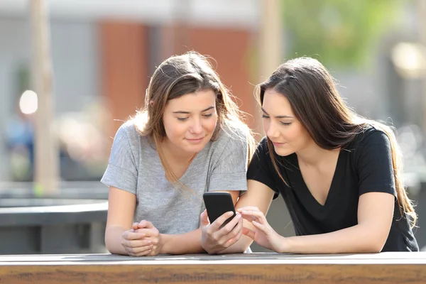 Dois amigos verificando o conteúdo do telefone inteligente em um parque — Fotografia de Stock