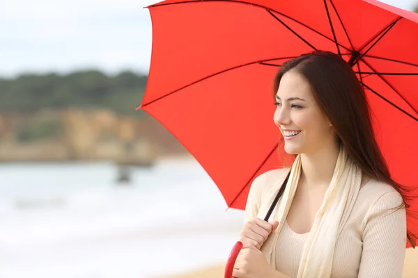 Mujer feliz mira a un lado sosteniendo paraguas rojo en la playa — Foto de Stock
