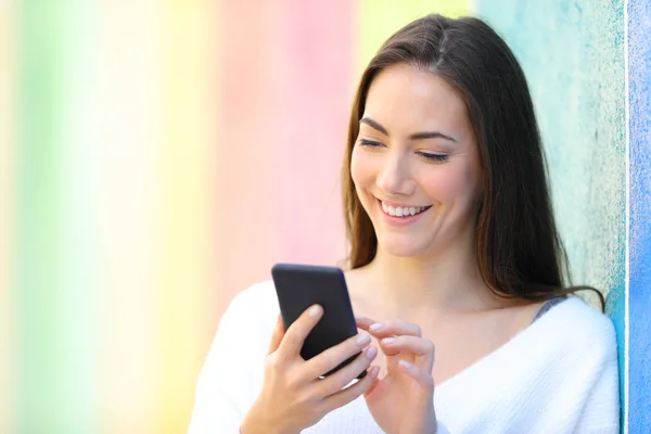Boldog nő használ szúró telefon-ban egy színes fal — Stock Fotó