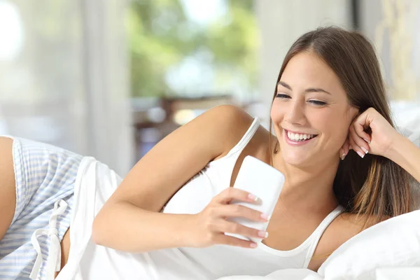 Woman lying on a bed at home using a smart phone — Stock Photo, Image