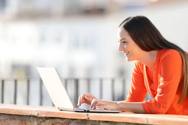 Lycklig kvinna skriver på laptop i en balkong — Stockfoto