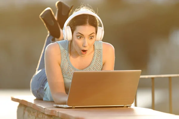 Здивована дівчина з ноутбуком для перевірки навушників — стокове фото