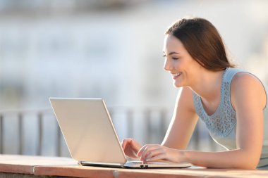 Mutlu kız bir balkon duvarı üstünde laptop üzerinde yazma