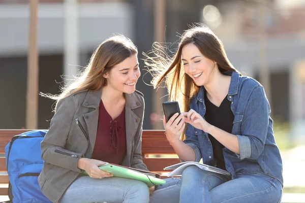 Glückliche Schüler checken Smartphone auf einer Bank — Stockfoto