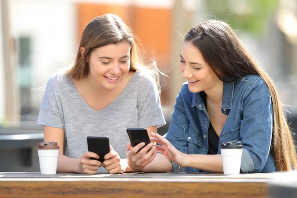 Två vänner jämföra sina smarta telefoner i en park — Stockfoto