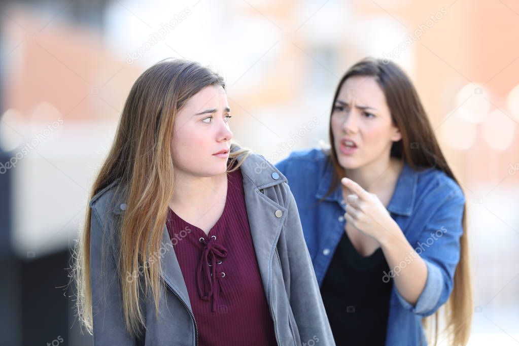 Angry girl scolding her confused friend in the street