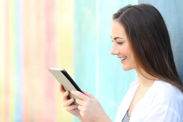 Ευτυχισμένο κορίτσι σε ένα πολύχρωμο τοίχο βλέποντας τα πολυμέσα στο tablet — Φωτογραφία Αρχείου