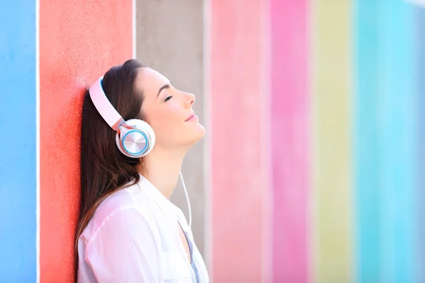 Avslappnad tjej lyssnar på musik som lutar i en färgglad vägg — Stockfoto