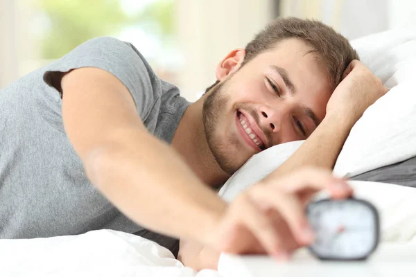 Happy man waking up turning off alarm clock — Stock Photo, Image