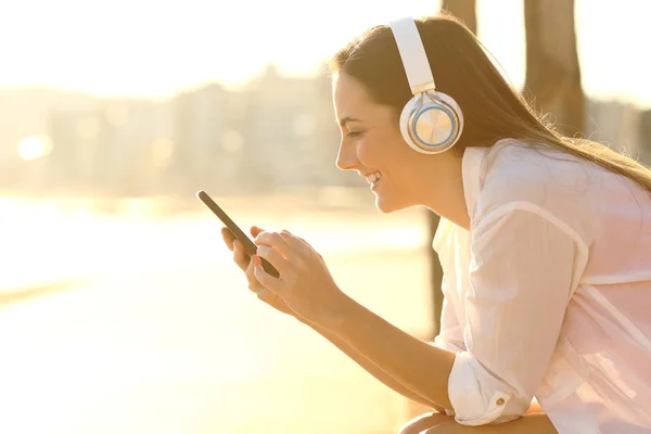 Happy girl listening to music downloads songs using phone — Stock Photo, Image