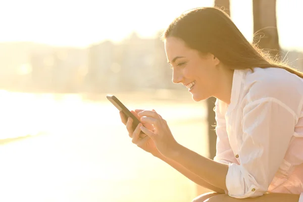 Szczęśliwa kobieta za pomocą inteligentnego telefonu na plaży miasta wybrzeża — Zdjęcie stockowe