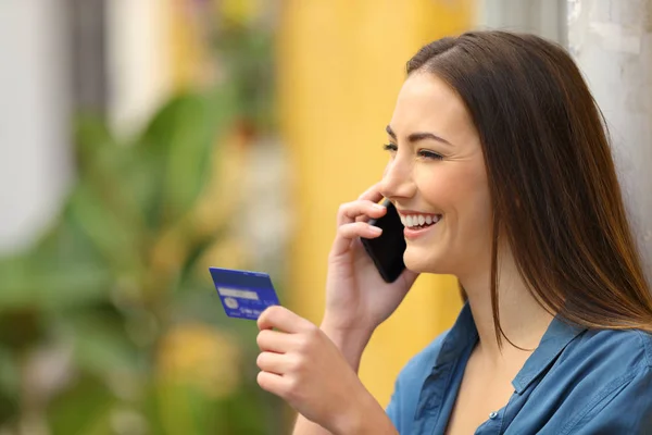 Mujer feliz hablando por teléfono sosteniendo una tarjeta de crédito — Foto de Stock