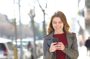 Mutlu genç sokakta bir akıllı telefon kullanarak yürüyor