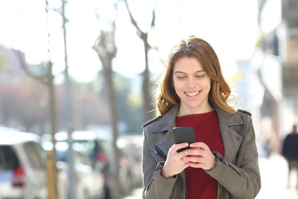 Felice adolescente cammina utilizzando uno smartphone per strada — Foto Stock