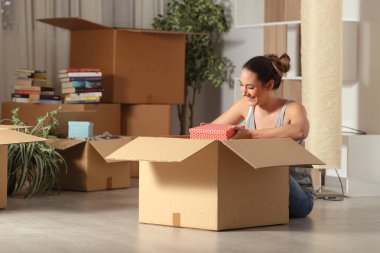 Happy woman moving home unboxing belongings in the night clipart