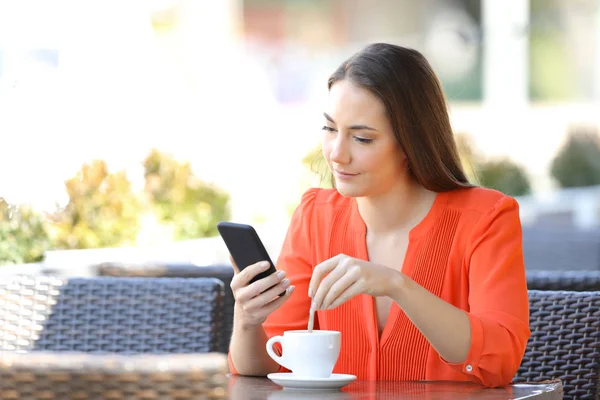 Frau rührt Kaffee und checkt Smartphone in Bar — Stockfoto