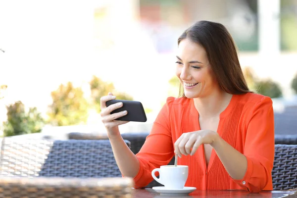 Mulher feliz assistindo vídeos no telefone em uma cafeteria — Fotografia de Stock
