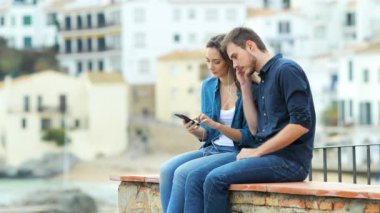 Tatilde bir çıkıntı üzerinde oturan bir akıllı telefon açık havada müzik paylaşımı Ciddi çift