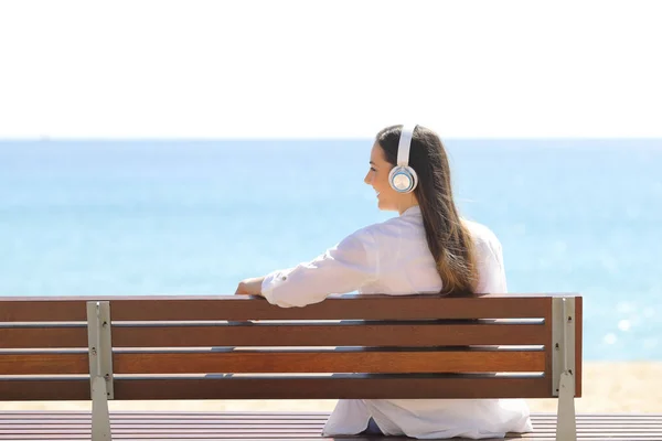 Menina feliz ouvir música em um banco na praia — Fotografia de Stock